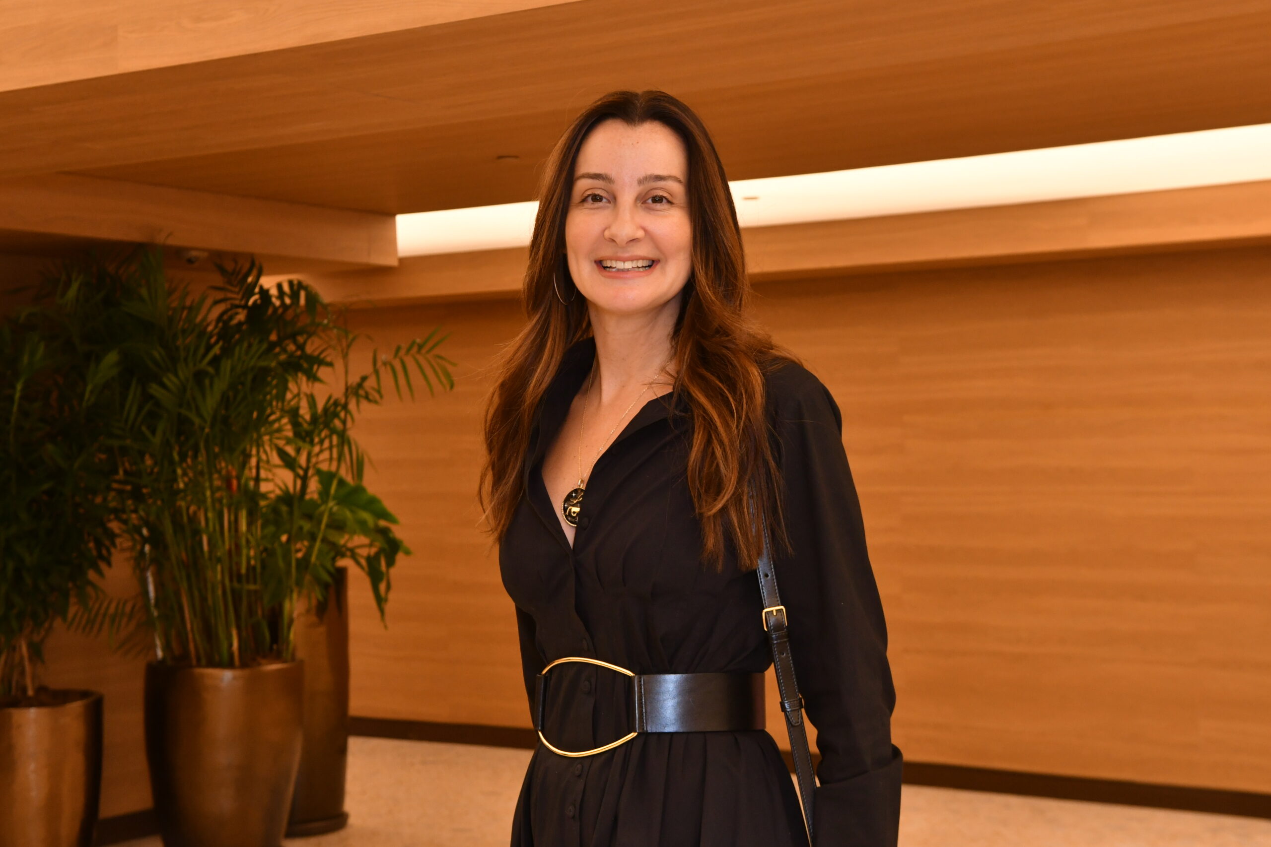 Mulher branca vestida de preto e de cabelos longos sorri para foto